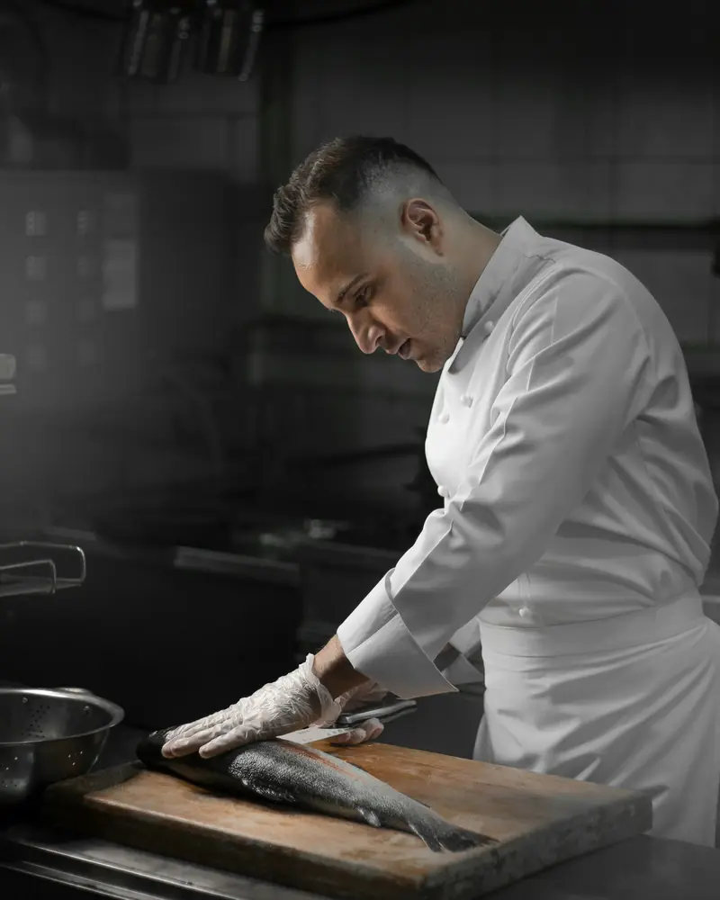 Cocinero limpiando un pescado sobre una tabla de madera